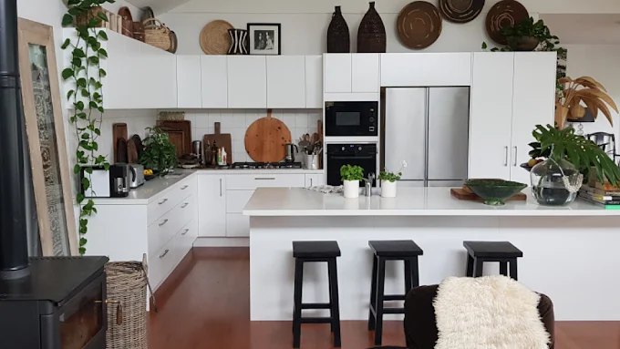 A finished open-plan kitchen with white flat-panel cabinets, a white stone island with bar stools, timber floors and a stainless steel fridge
