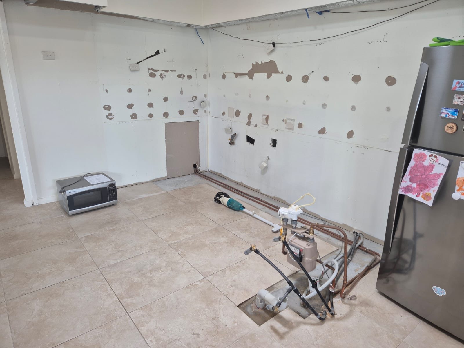 A kitchen stripped back to bare walls and tiled floor mid-renovation, with plumbing and wiring exposed