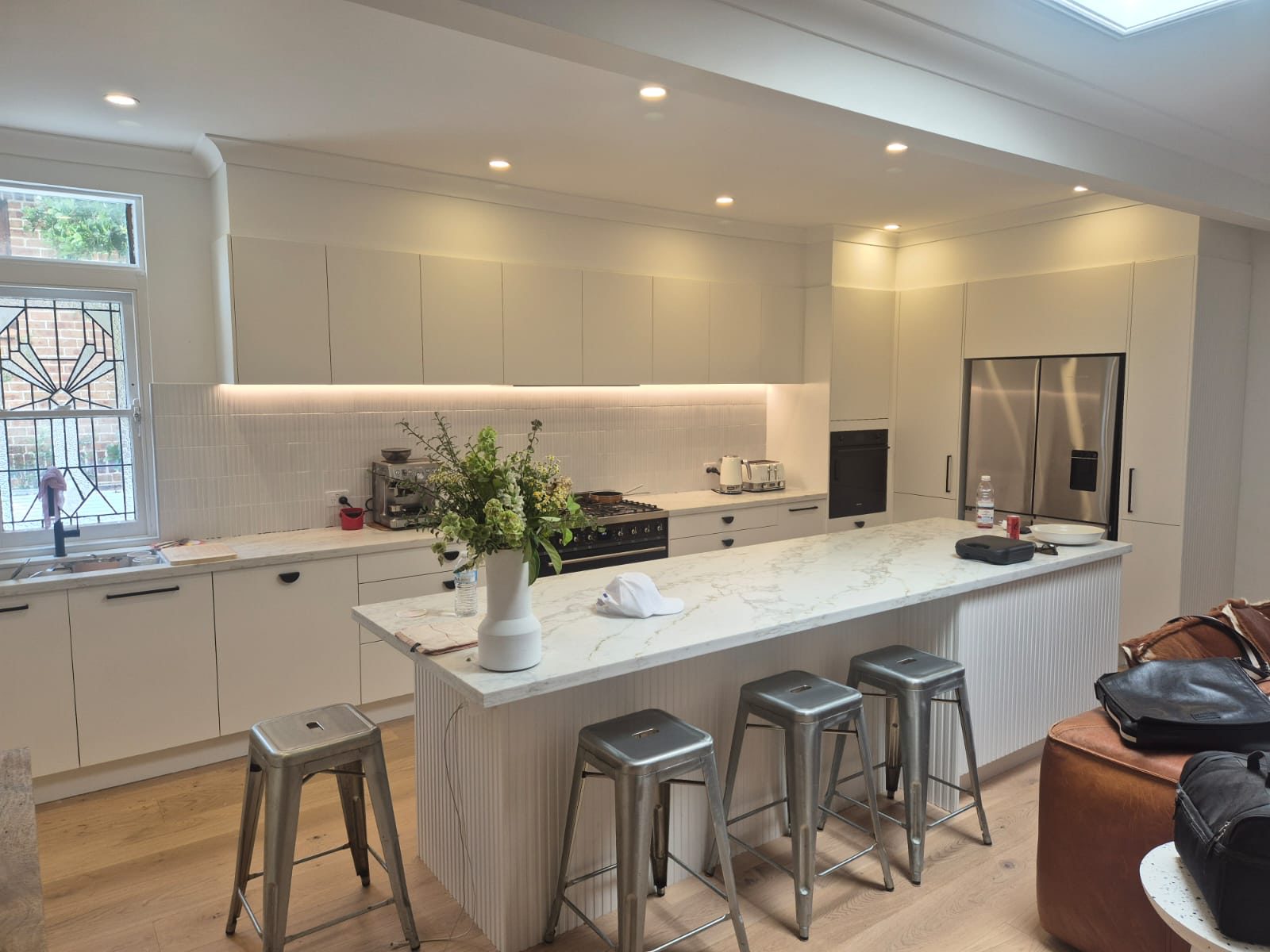 A finished kitchen with an off-white fluted island, marble-look benchtops, a dark range cooker and a stainless steel fridge