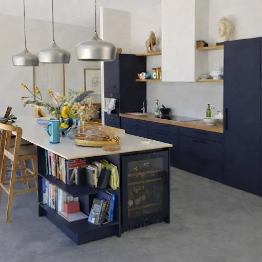 An open-plan kitchen with deep navy cabinetry, timber benchtops, an island with open display shelving and three dome pendants